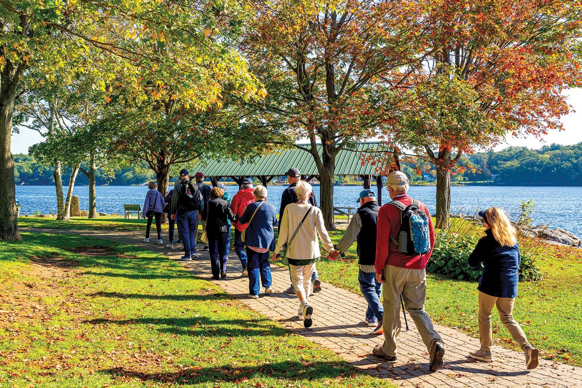 A group of guests on a guided walk along a lakeside path beneath trees in autumn color