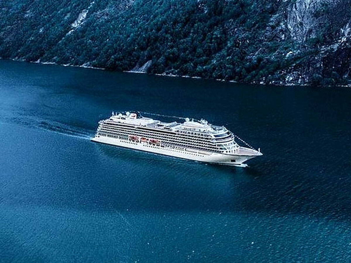 Viking Vela sails through a deep blue fjord framed by steep, forested cliffs
