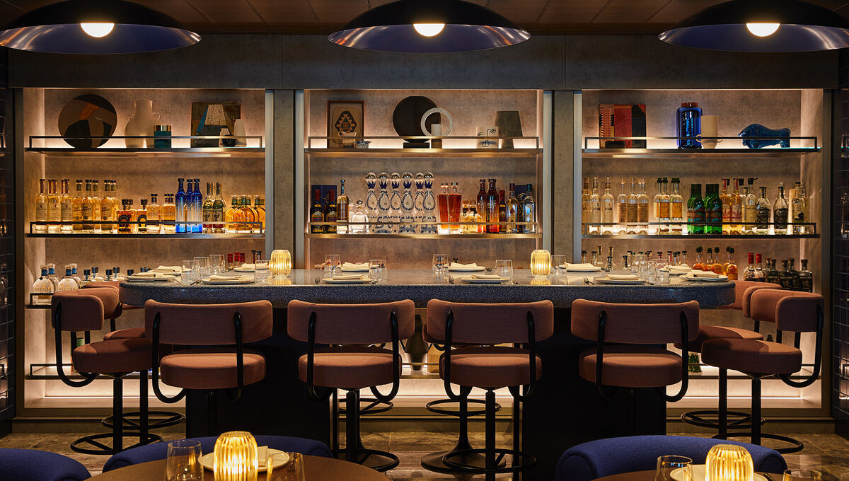 The moody, candlelit bar at Pink Agave aboard a Virgin Voyages ship, lined with backlit shelves of mezcal and tequila