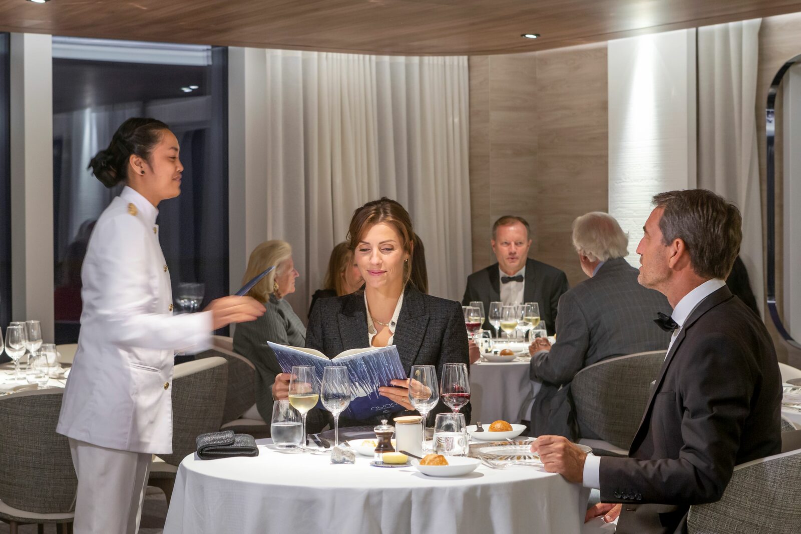Guests in evening attire peruse menus at elegantly set tables inside the fine-dining restaurant aboard Ponant's Le Commandant Charcot