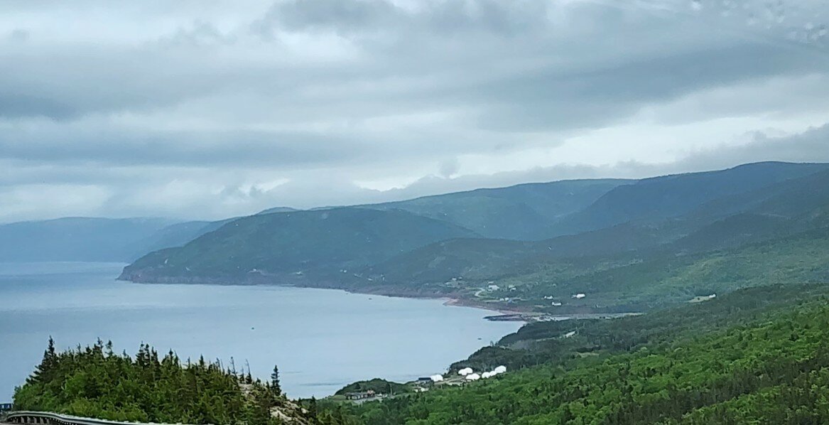 Green highlands sweep down to the coast under moody clouds along the Cabot Trail on Cape Breton