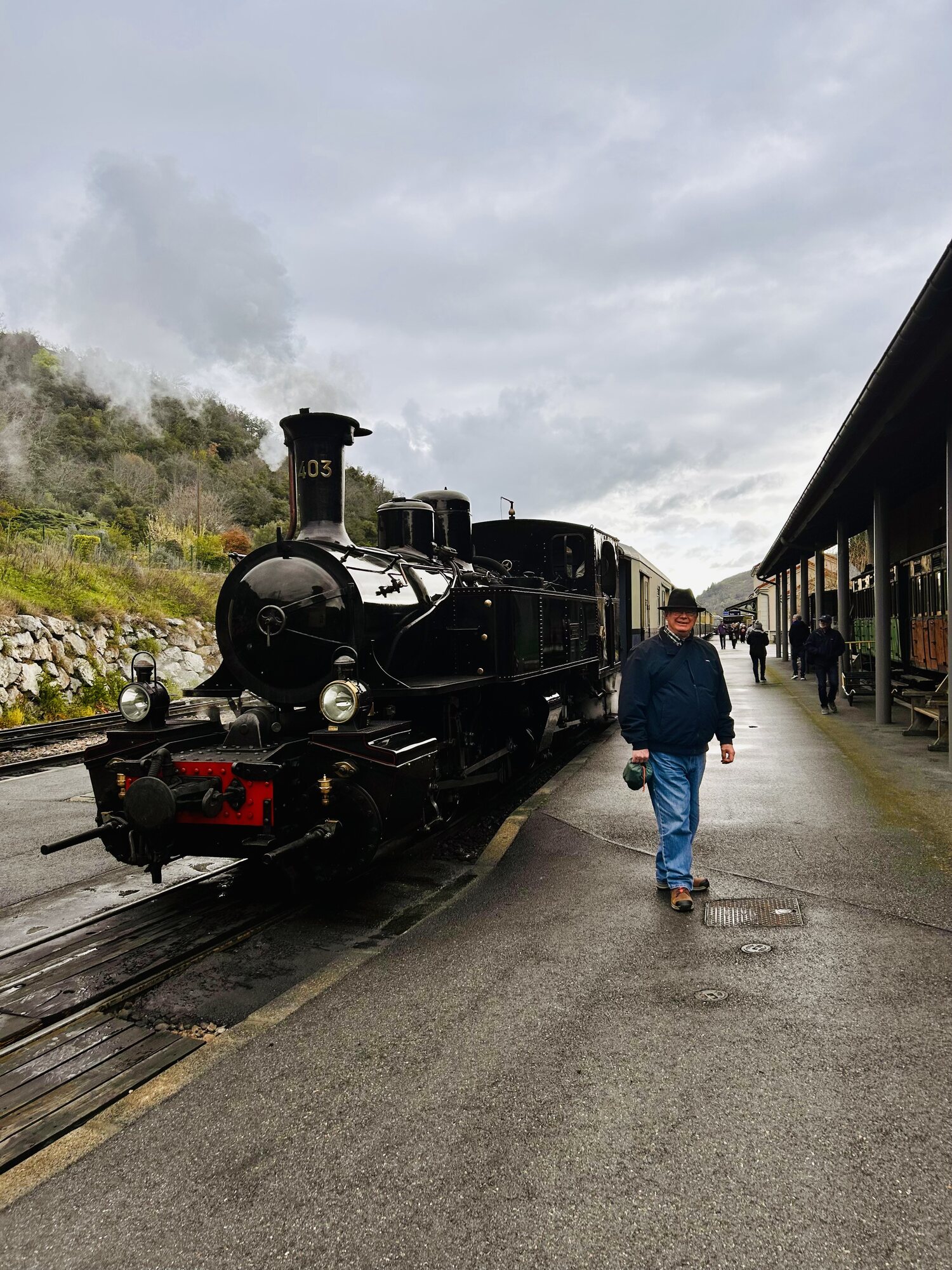 Lewis stands on the platform beside the vintage steam locomotive of the Train des Gorges near Tournon