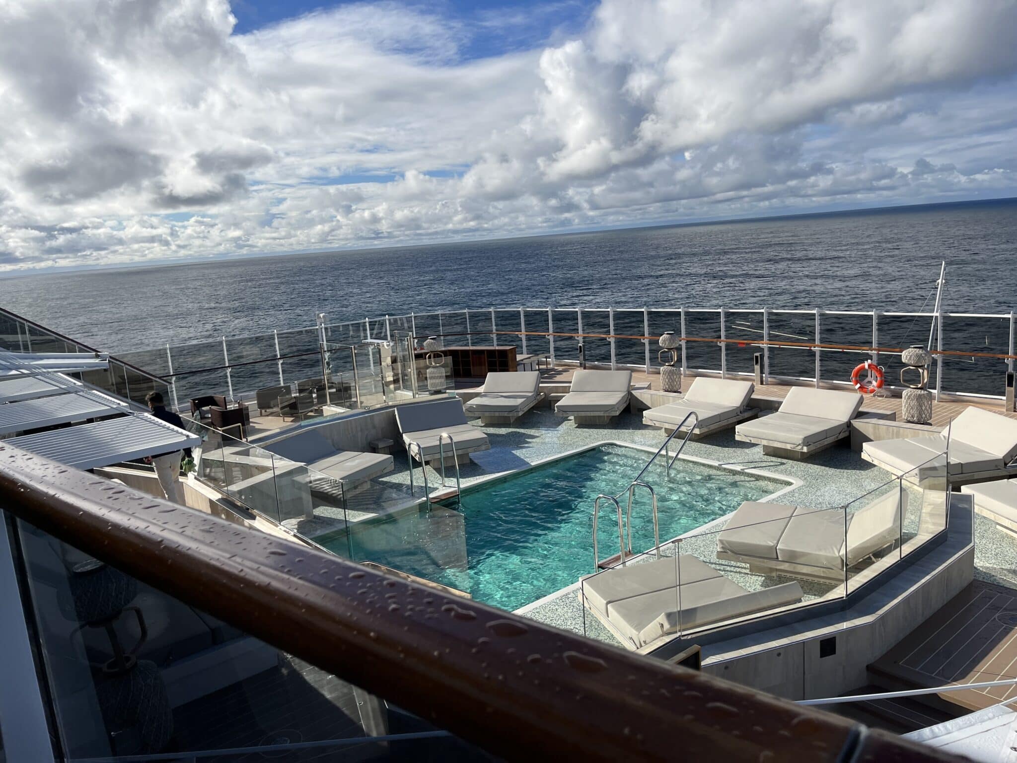 Outdoor pool deck aboard Explora Journeys with cushioned lounge chairs overlooking the open ocean