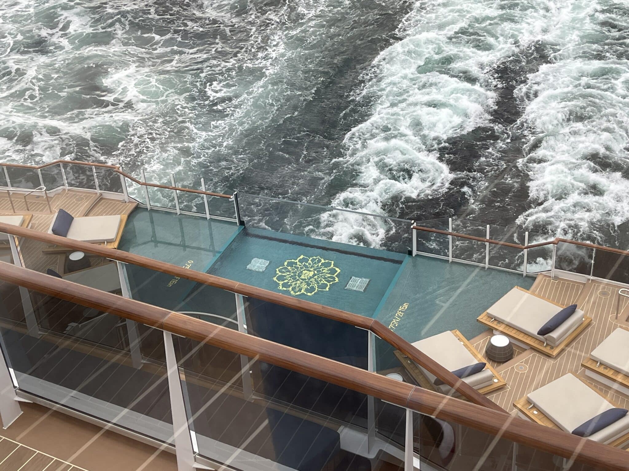 Stunning glass-walled infinity pool at the stern of Explora Journeys viewed from above with ocean wake beyond