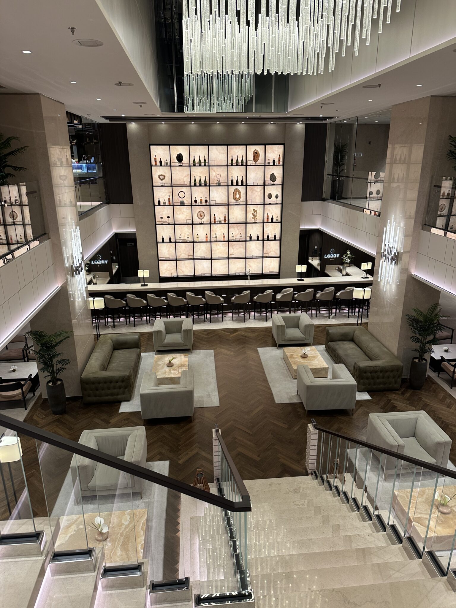The grand Lobby Bar aboard Explora Journeys with double-height atrium, cascading chandelier, and backlit wall of fine spirits